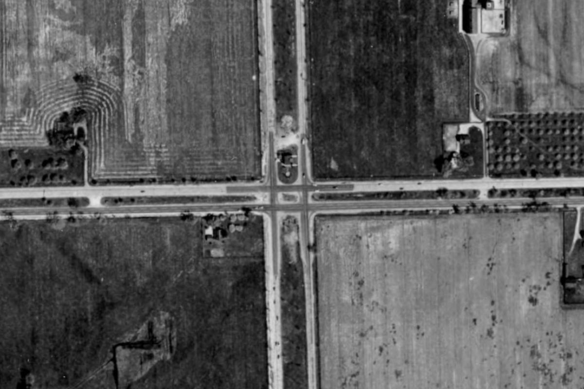 The same crossing in 1949: a two-lane crossroads between open fields